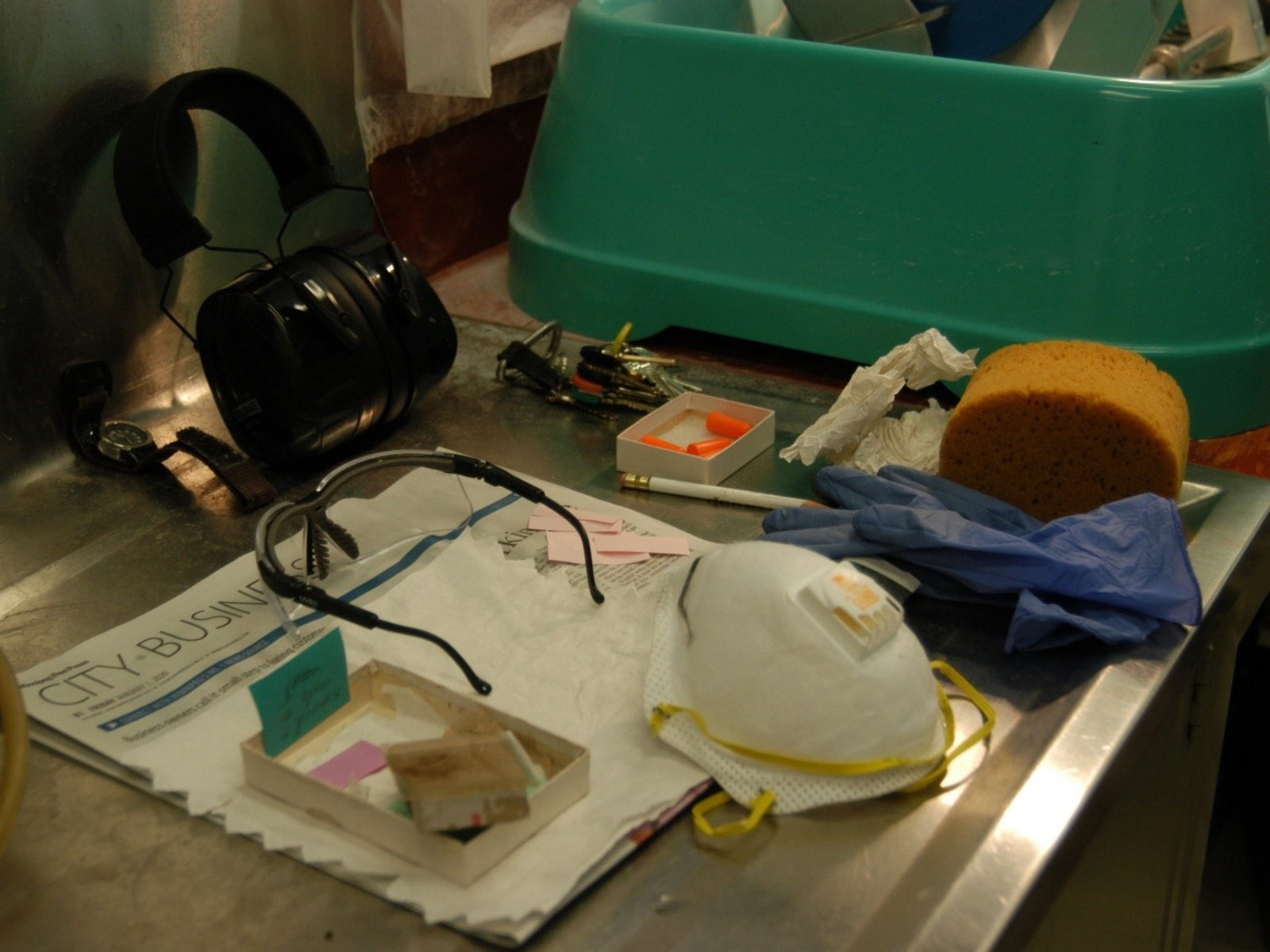 A work station set up with various tools and equipment including earplugs, ear muffs, safety glasses, blue rubber gloves, a sponge, and a high-quality face mask.