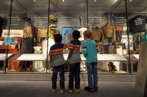 From behind, three children standing together looking into a wall of display cases filled with artifacts.