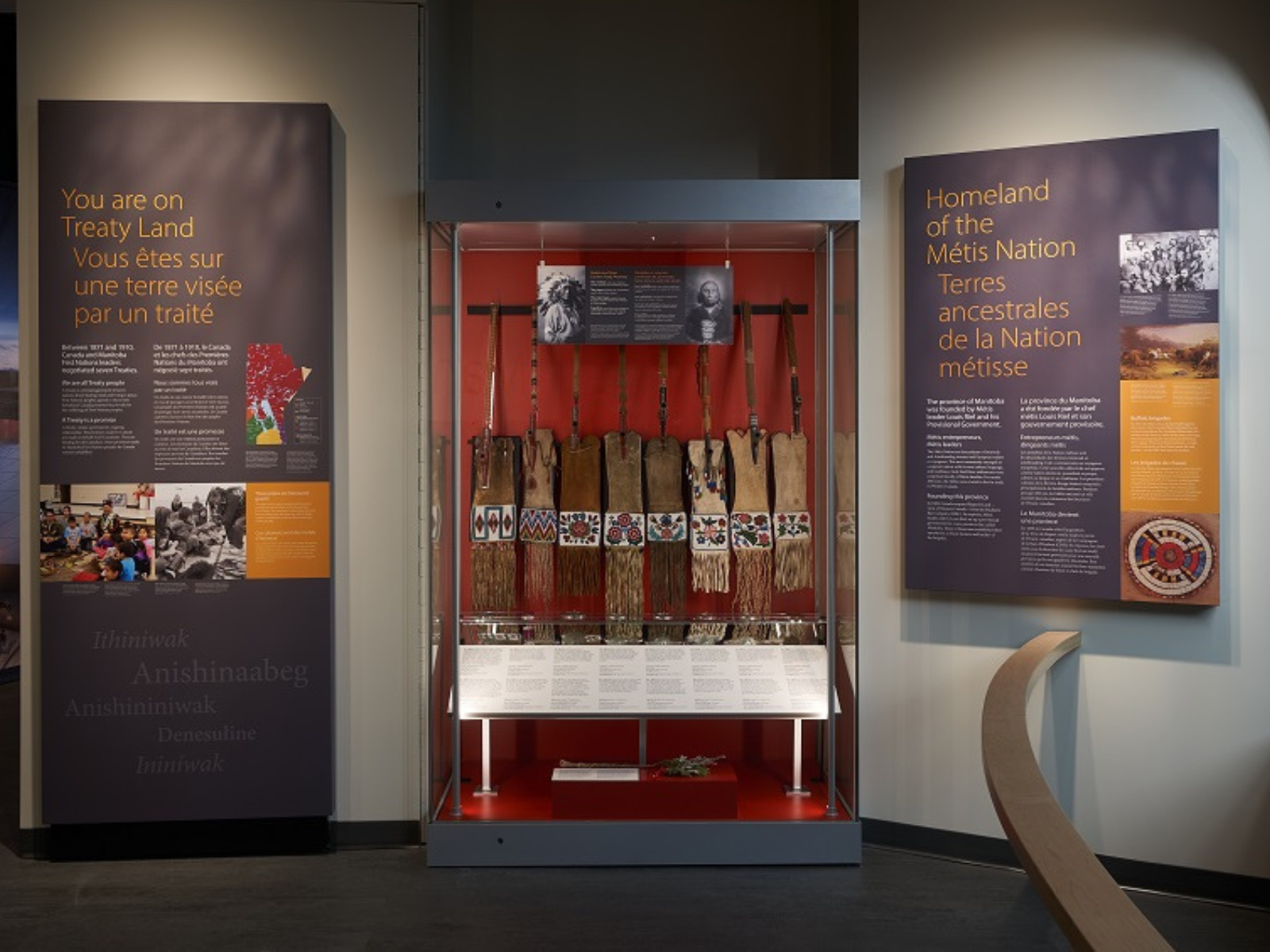 A display case with medals, pipes, and pipe bags. To the left of the case, a text panel is titled, "You are on Treaty Land", and to the right a text panel is titled, "Homeland of the Metis Nation".
