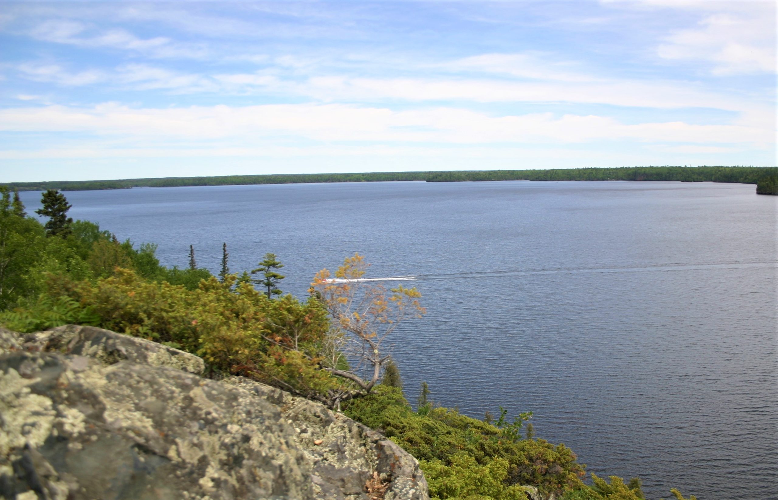 View from a rocky ledge looking out over a lake. The far bank is visible in the distance.