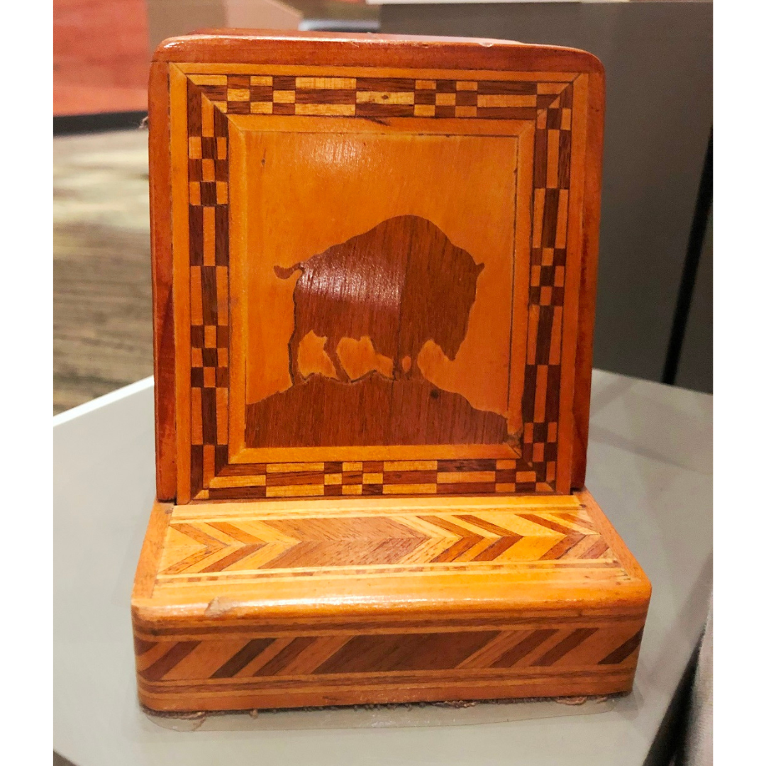 A wooden bookend made of wood of varying shades of brown and orange. On the front is a bison on a hill top.