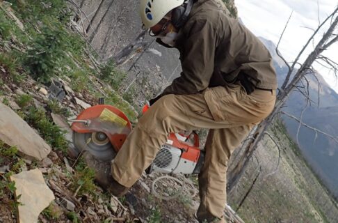 Joe Moysiuk standing on a rocky ledge, holding a rock saw. The saw blade is slicing through a piece of shale.