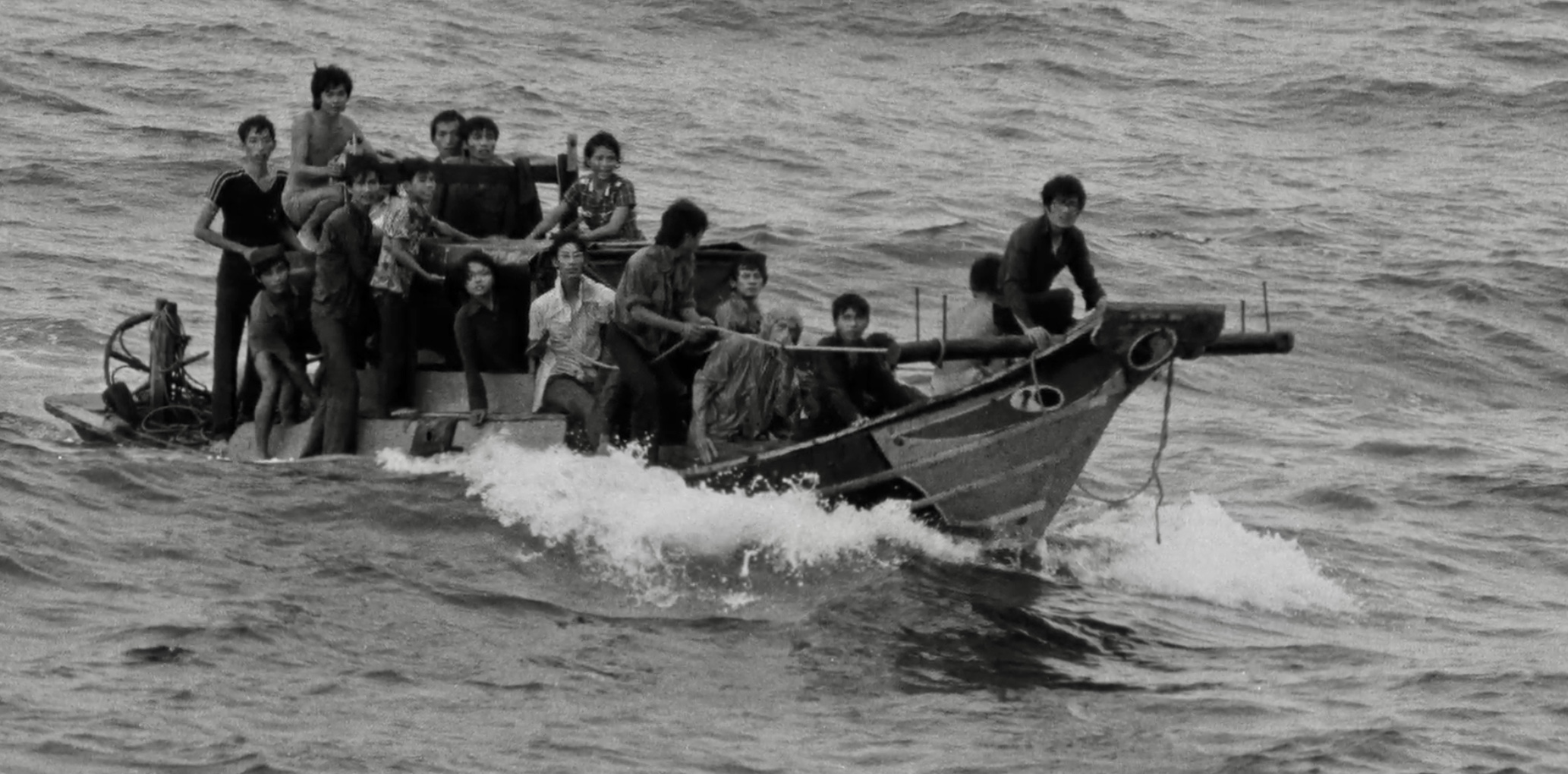 A black and white photograph of a group of refugees on a small boat in the water.