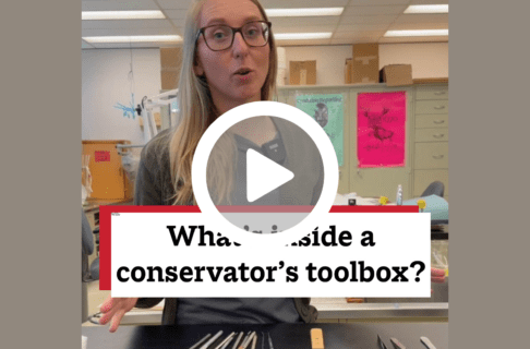 A screenshot of a video, an individual standing in a labin front of a table with a variety of tools laid out in front of them. There's a play button over the screenshot and overlaid text reads, "What's inside a conservator's toolbox?".