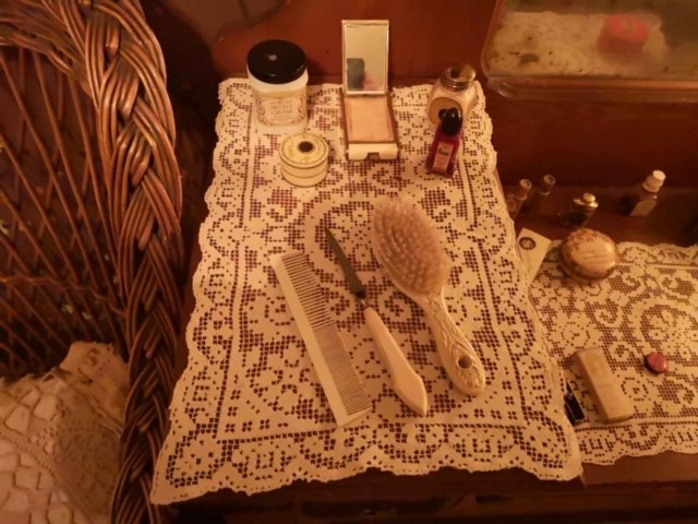Close up view at a portion of a dressing table. Laid out on a daily are a hairbrush, comb, and hair-pick, as well as several creams and powders.