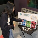 A youth placing a game piece on a game board labelled "Trash Sorting Activity".