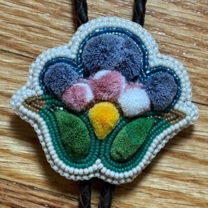 A colourful brooch in a floral shape with beaded edging and tufted detailing on the inside.