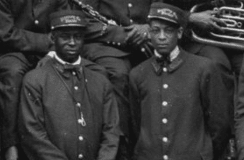 A black and white photograph of two Black men in matching uniforms and hats standing side by side.