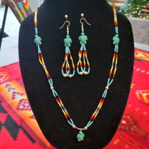 A set of beaded earrings and necklace in red, yellow, white, black, and blue beads with turtle accent beads, on a jewelry bust.