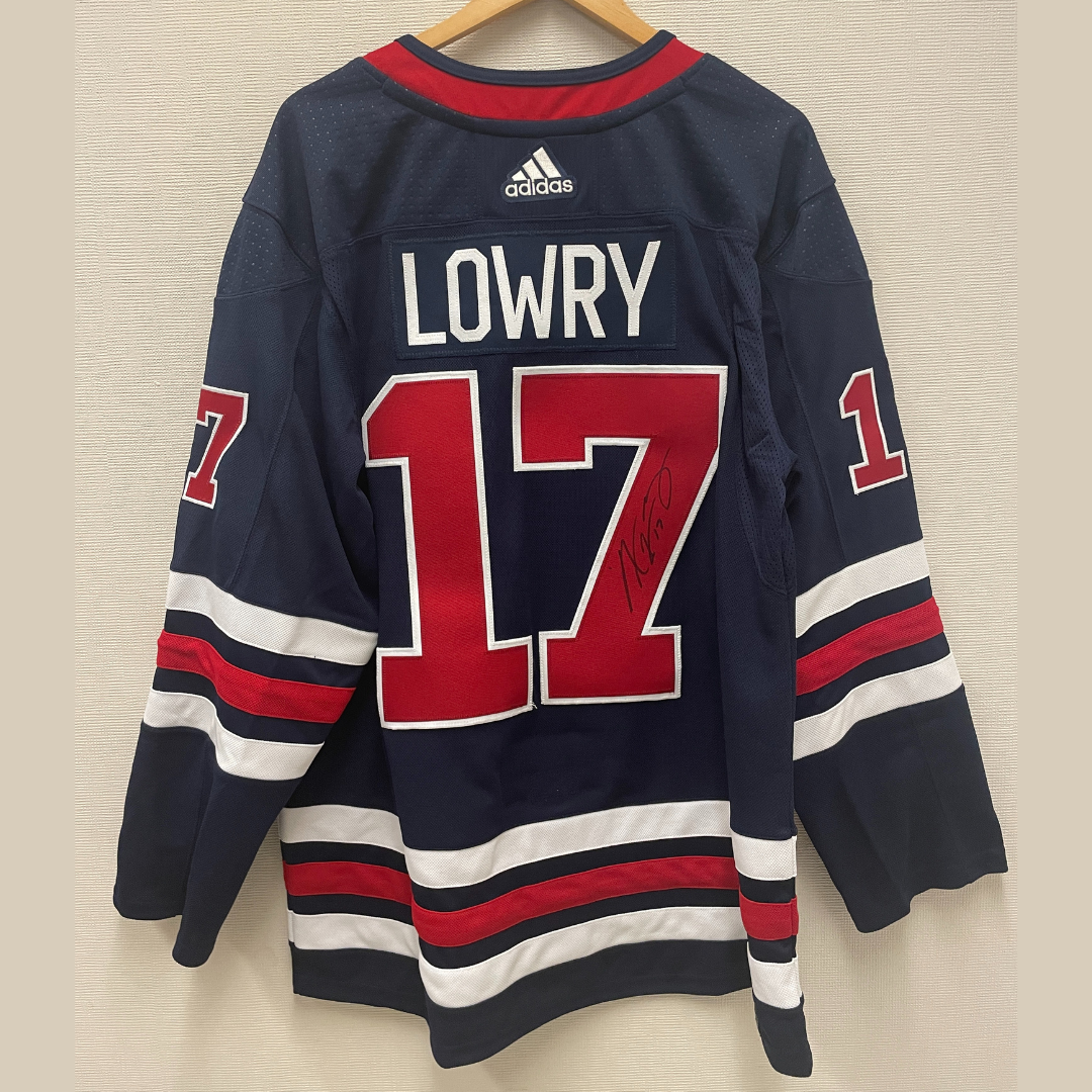 Dark blue jersey with red and white accent stripes hanging on a hanger. Along the top is stitched the name "LOWRY" followed by a red number 17, with an autograph in the bar of the 7.