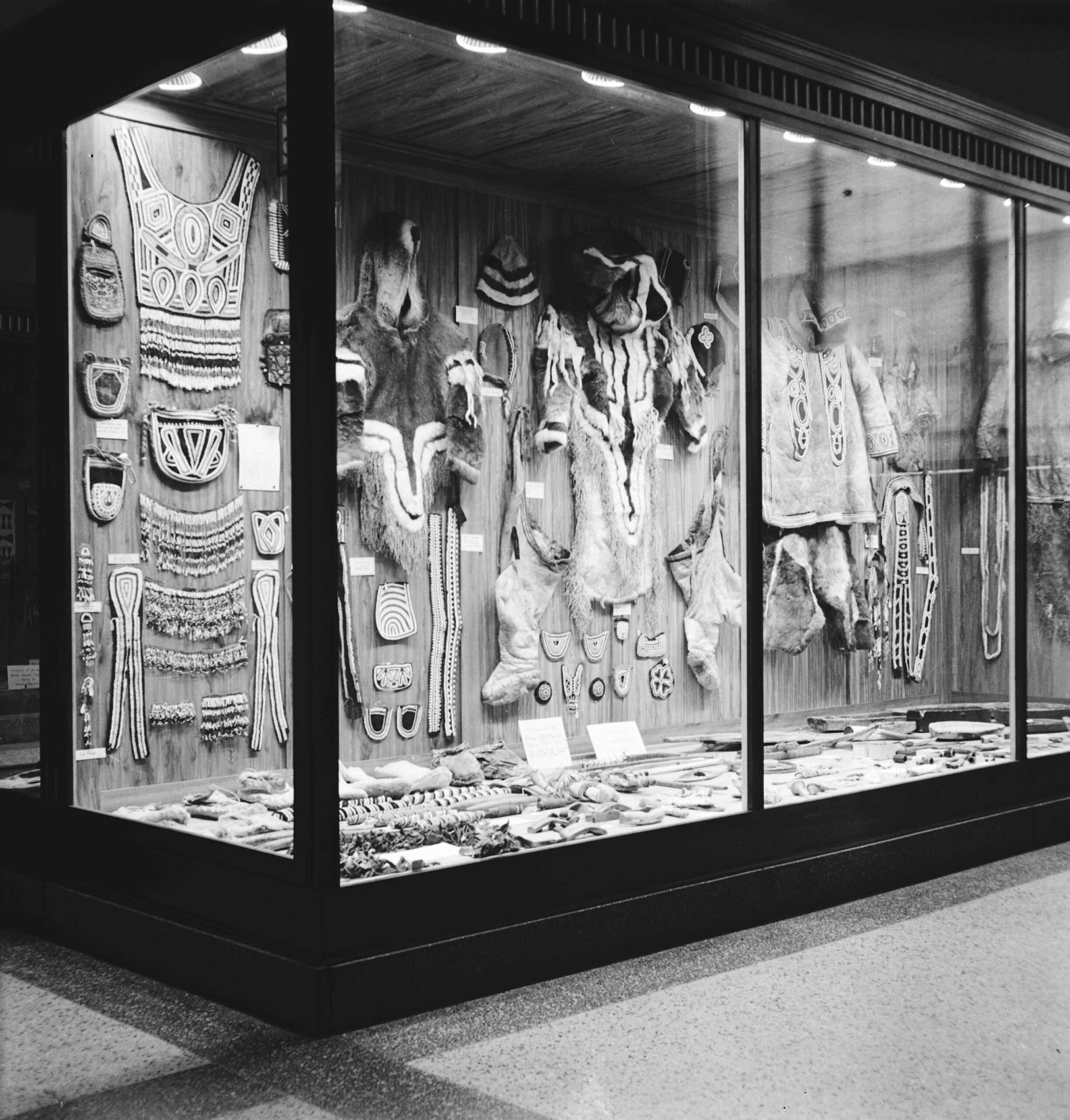 Black and white image of a museum display case housing various Indigenous artifacts. 