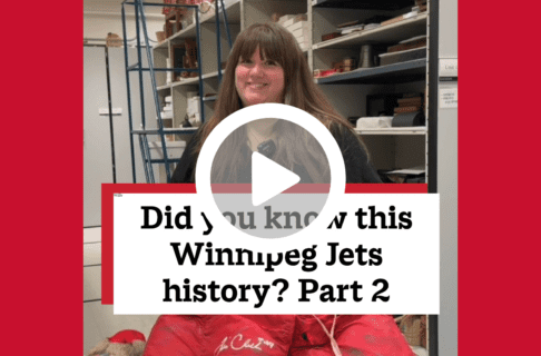 A screenshot of a video, an individual standing in museum collection storage holding up a red pair of hockey goalie's shorts. There's a play button over the screenshot and overlaid text reads, "Did you know this Winnipeg Jets history? Part 2".