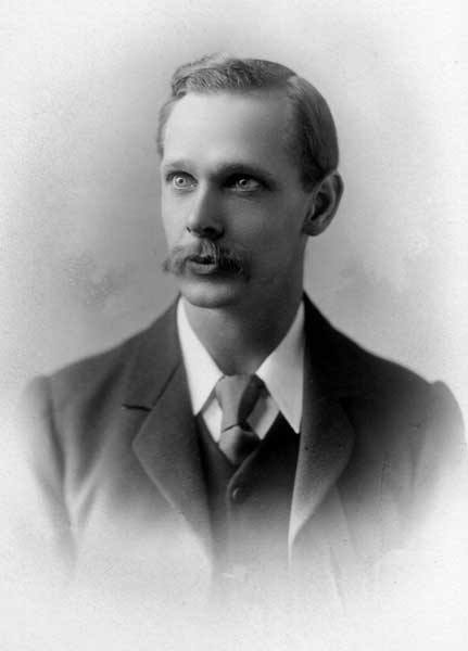 Formal black and white photograph of a man with neatly arranged hair and a kempt moustache wearing a three-piece suit.