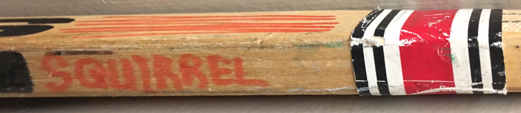 Close-up on the wooden handle of a hockey stick with SQUIRREL written in it in red marker.