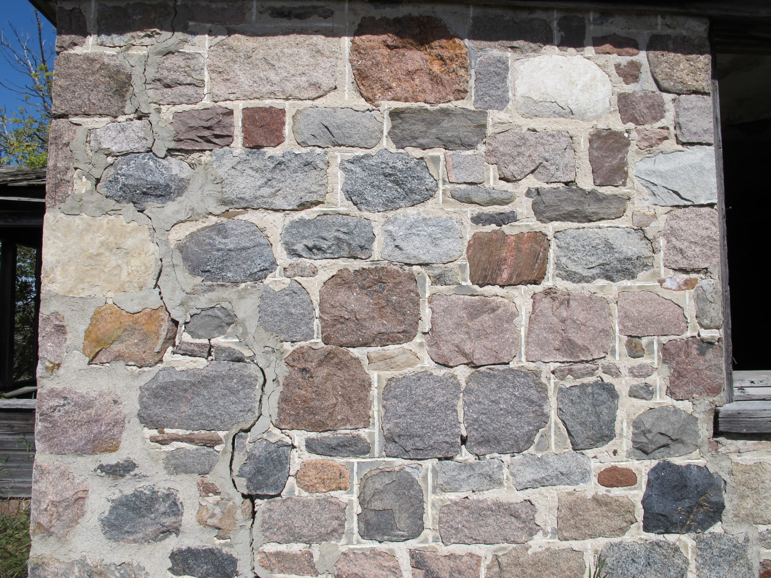 A close-up of a stone wall with stone blocks of varying shades of grey and brownish-red.