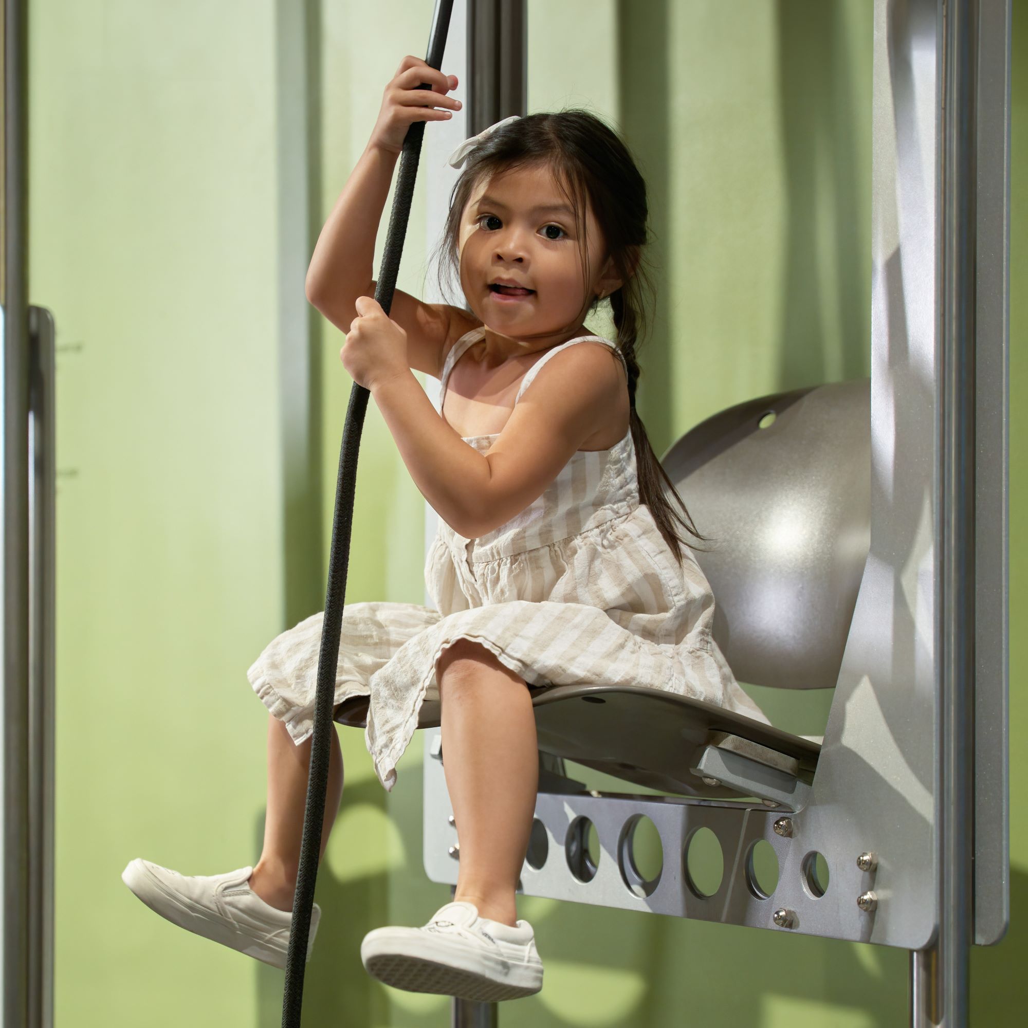 A child pulling themself up in a pulley chair in the Manitoba Museum Science Gallery.