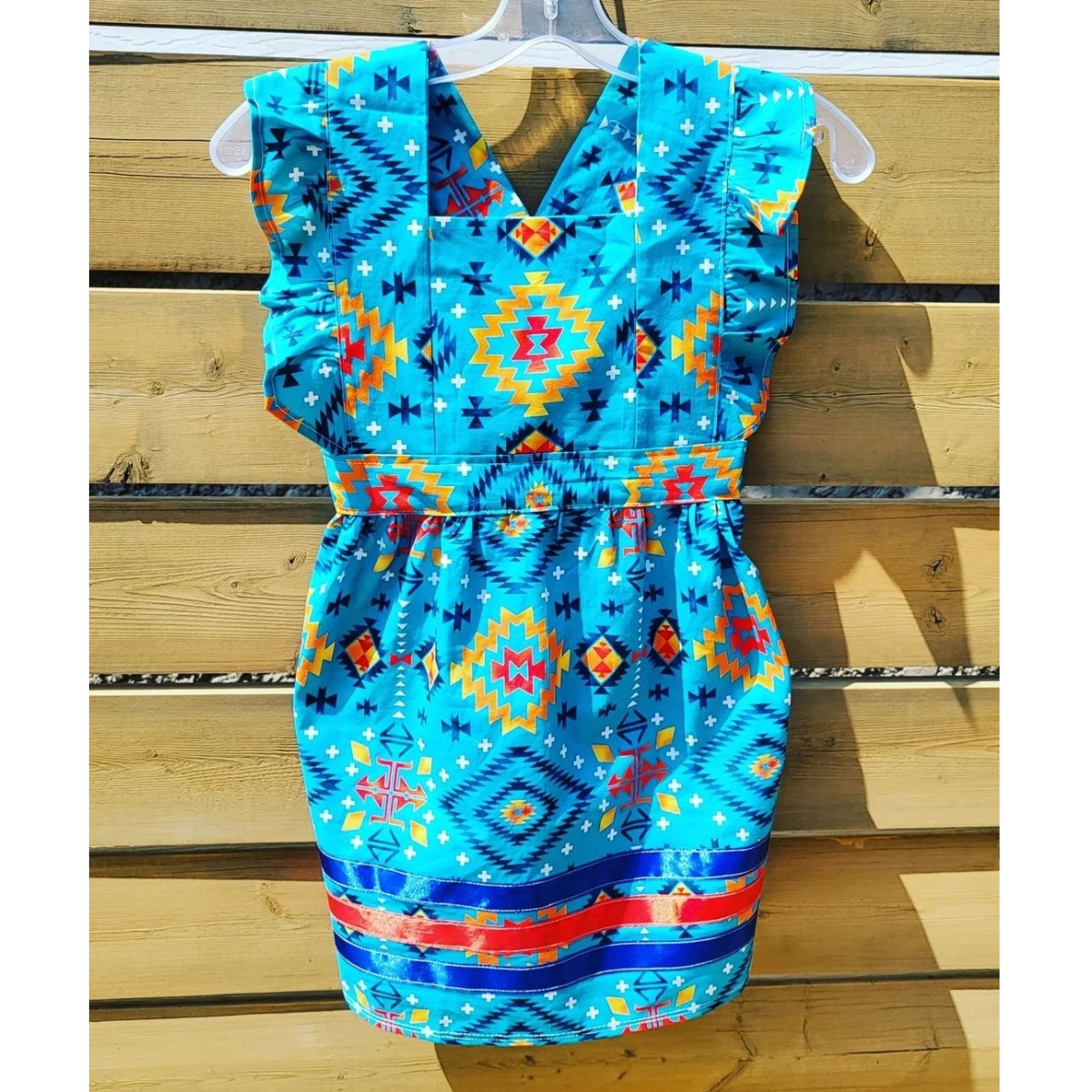 A toddler-sized patterned dress with ruffled sleeves and red and blue ribbons along the bottom.
