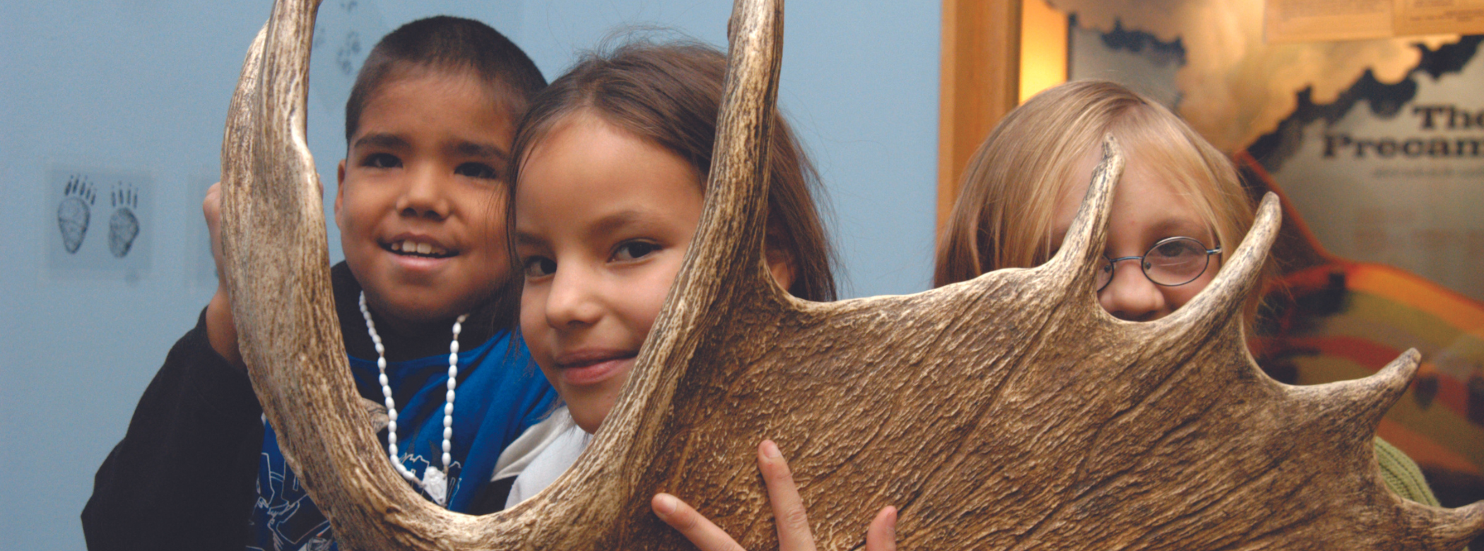 A three students peer at the camera through a moose antler.