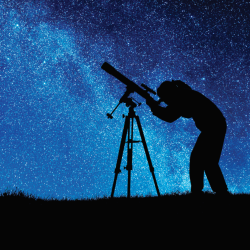 Photograph of an individual looking into a telescope silhouetted against a starry night sky.