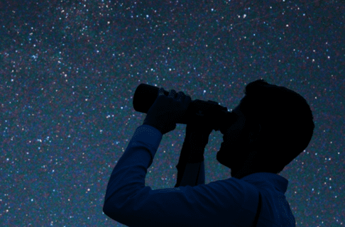 A person looks at a starry night sky with binoculars.