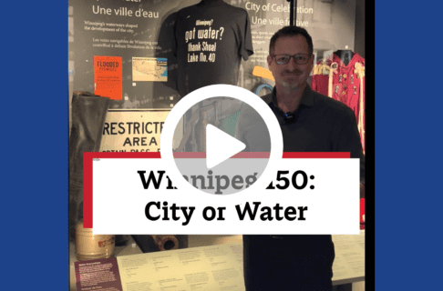 A screenshot of a video, an individual standing in front of a display case containing a number of artifacts including a black t-shirt reading "Winnipeg? Got water? Thanks Shoal Lake No 40". There's a play button over the screenshot and overlaid text reads, "Winnipeg150: City of Water".