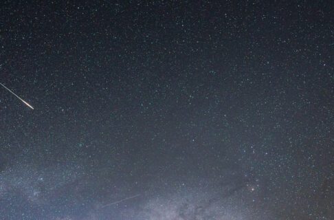 A meteor flashes across a starry sky.