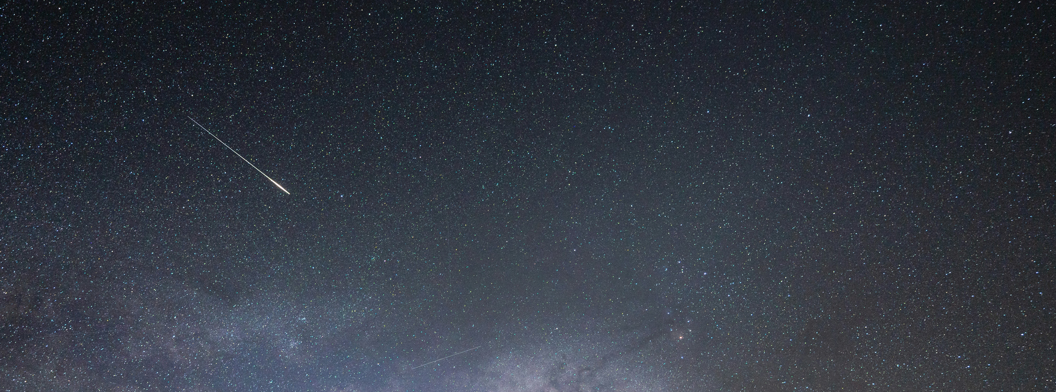 A meteor flashes across a starry sky.