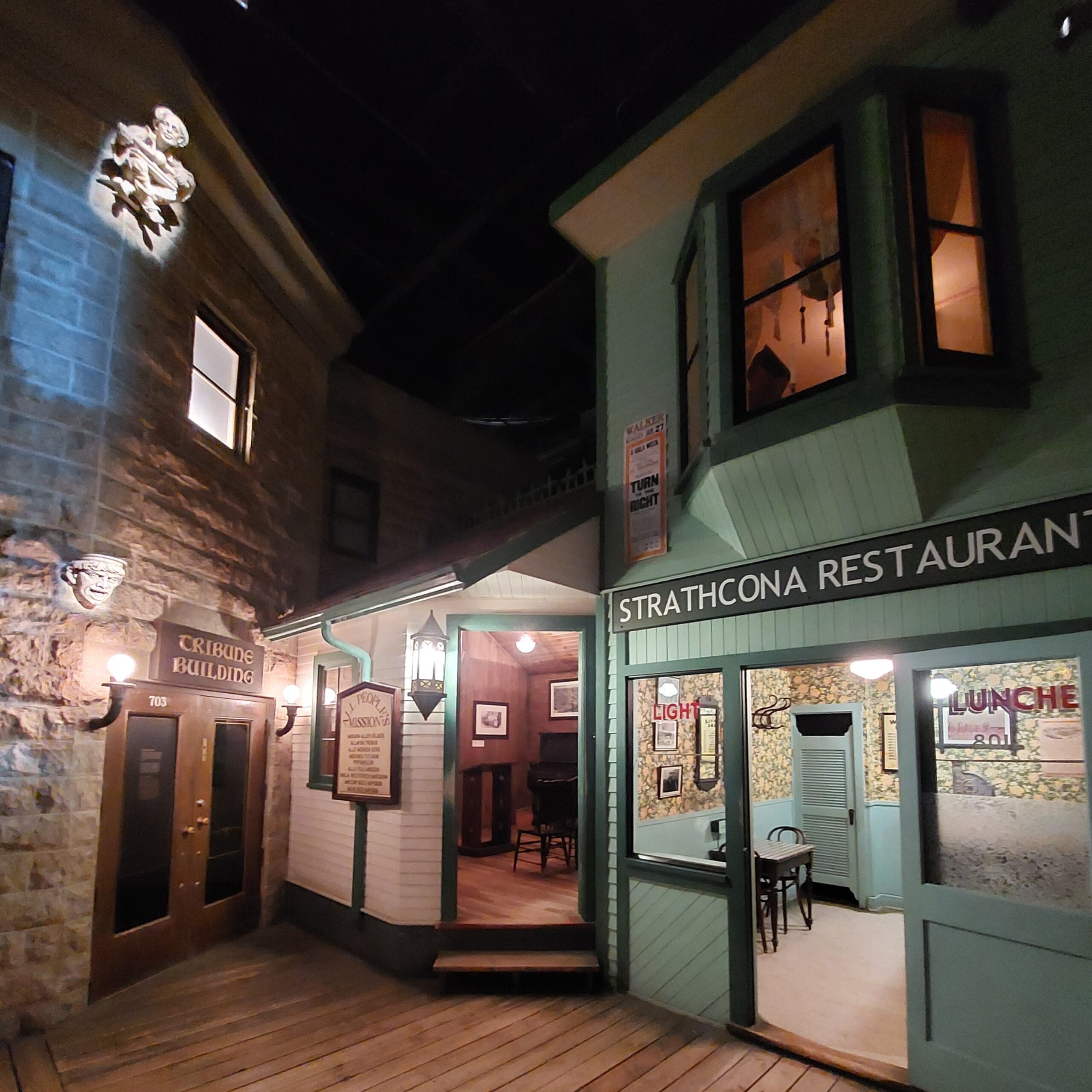 Looking down a recreated historical boardwalk in a fully immersive museum diorama. From left to right are the Tribute Building, All People's Mission building, and Strathcona Restaurant.