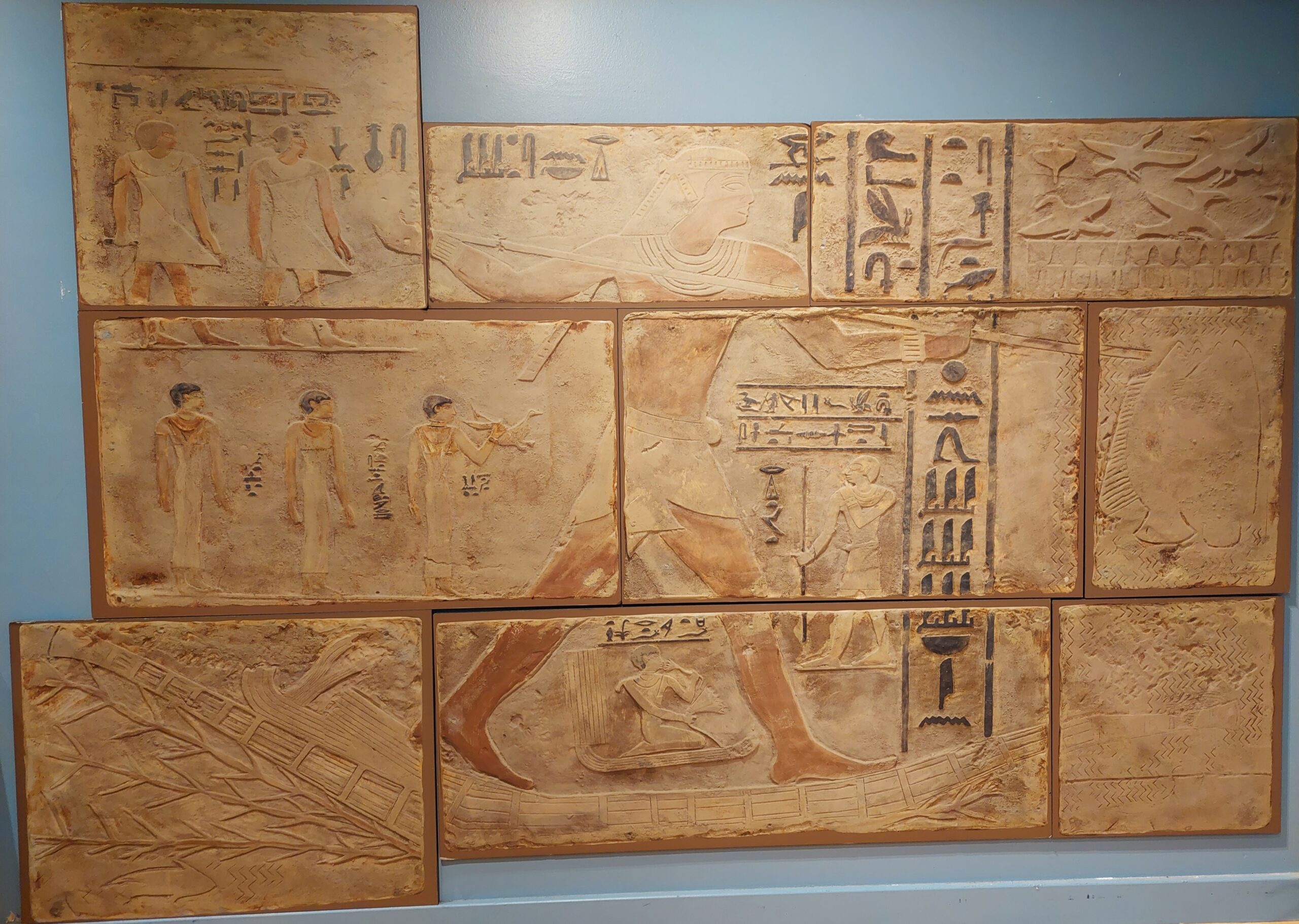 A reproduction of an Egyptian tomb wall. Nine tiles show a number of figures and hieroglyphics.