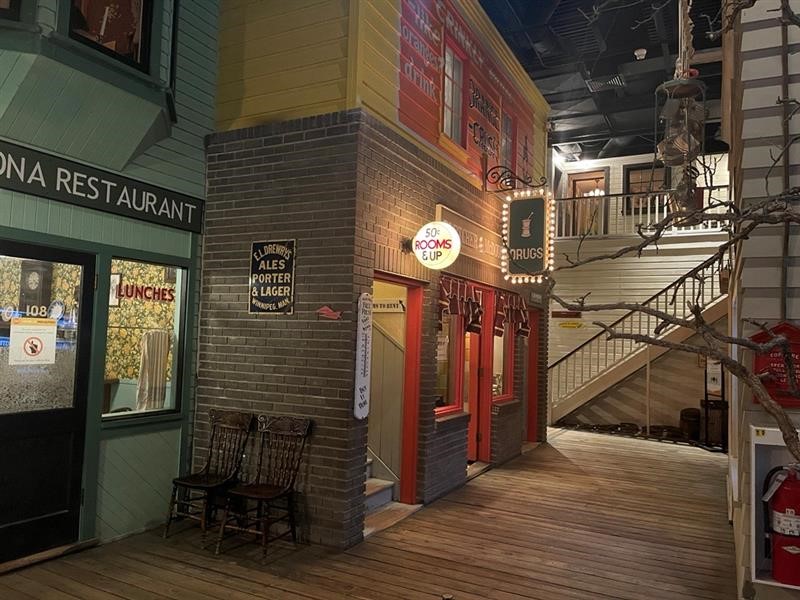 Looking down a recreated historical boardwalk in a fully immersive museum diorama. On either side of the boardwalks are shops and stairs leading up to a second level.