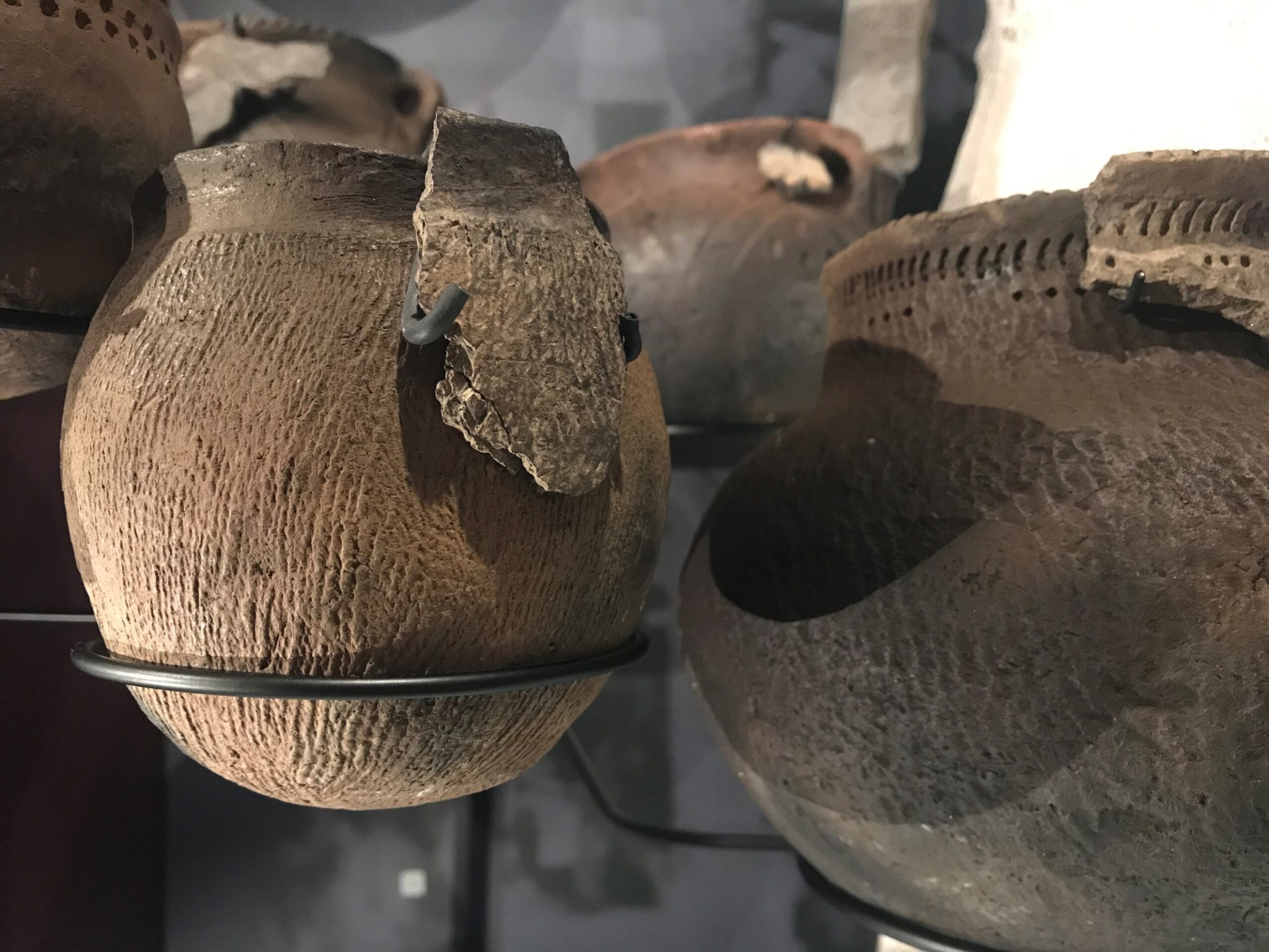 Close up on a pottery artifact on a stand in a Museum display case. A portion of the original pot is displayed over the full recreation.