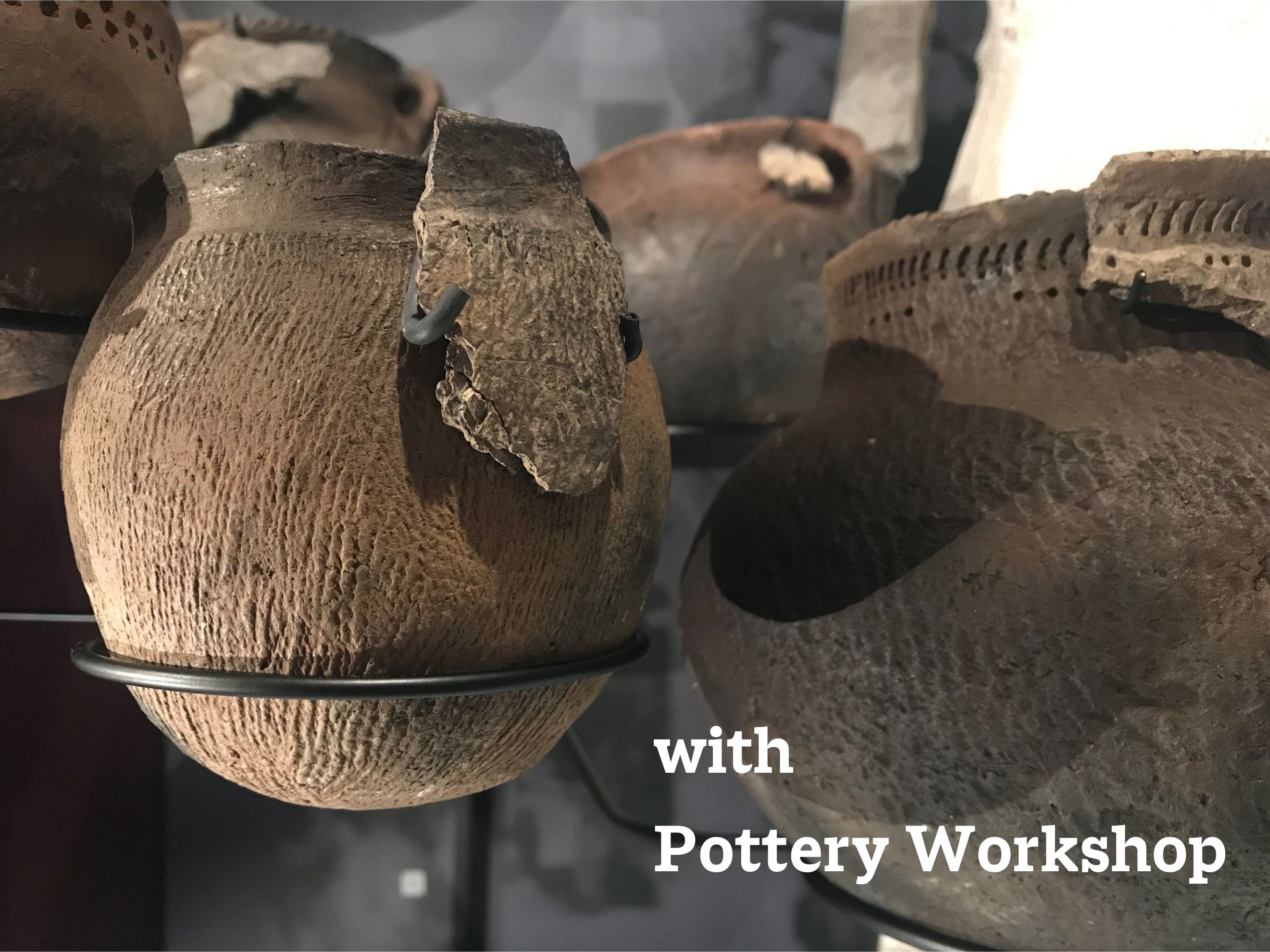 Close up on a pottery artifact on a stand in a Museum display case. A portion of the original pot is displayed over the full recreation. Text in the bottom right corner reads, "with Pottery Workshop".