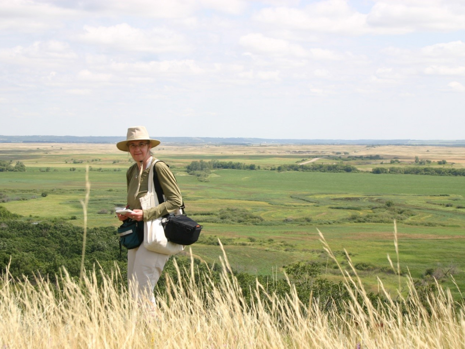 Dr. Diana Bizecki Robson on the grassy bank of a hill overlooking vast prairie.