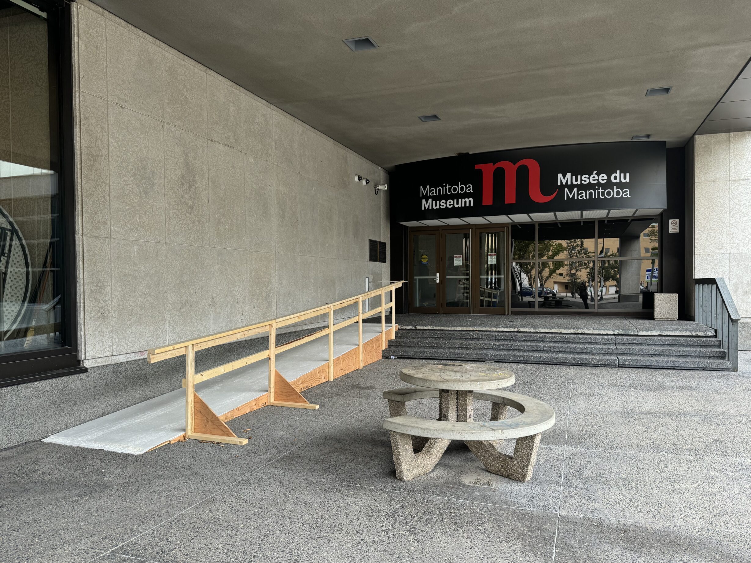 A plywood access ramp at one end of a staircase leading to the Manitoba Museum's Main Street entrance.