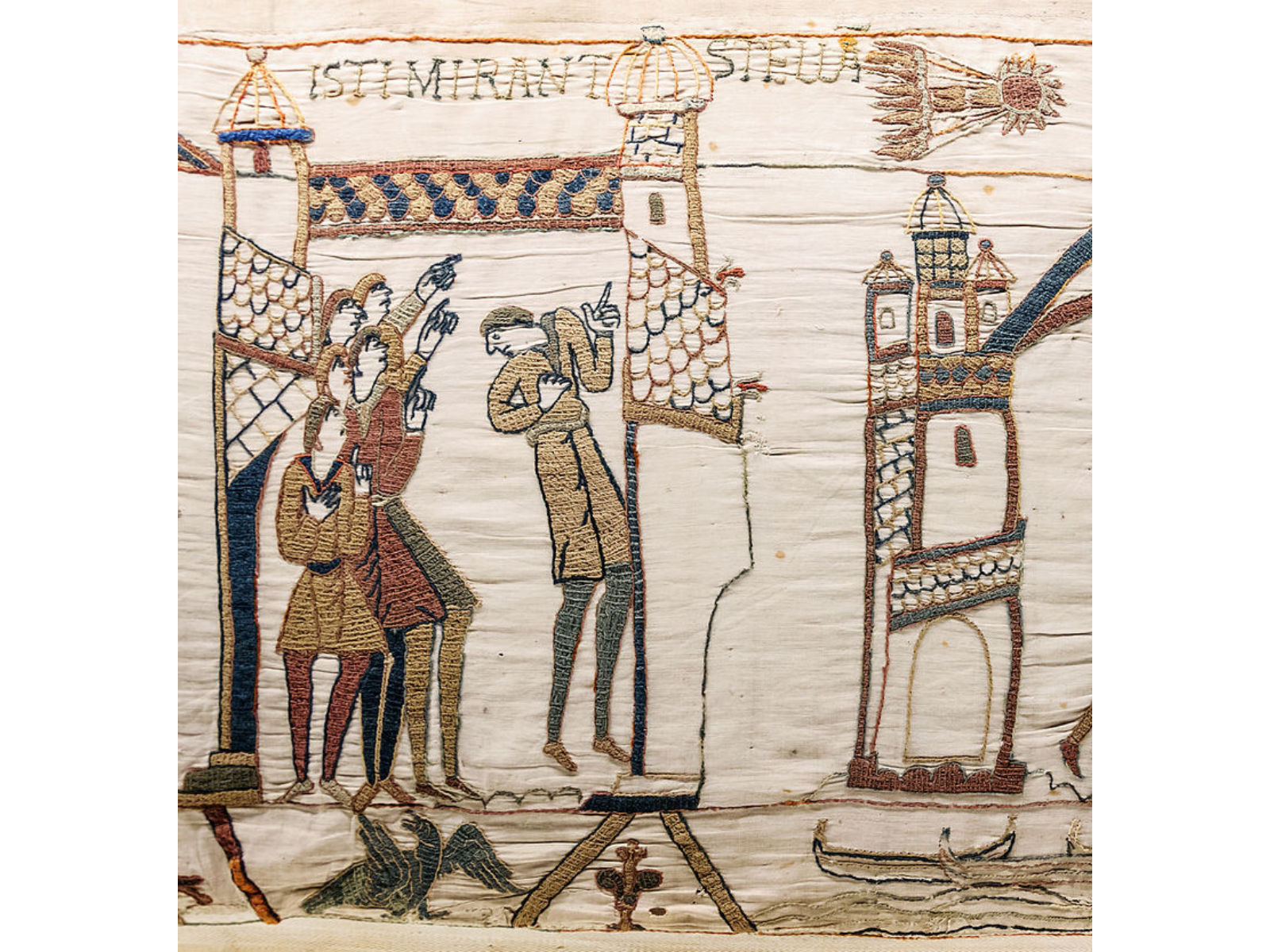 A close look at an embroidered tapestry showing a small group of people pointing up towards a comet streaking across the sky.