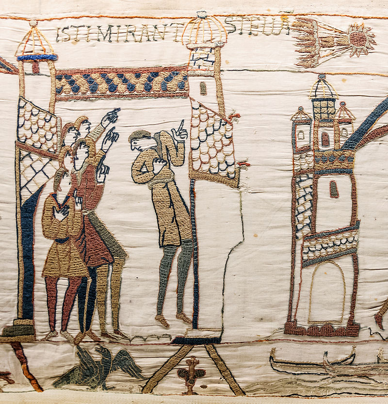 A close look at an embroidered tapestry showing a small group of people pointing up towards a comet streaking across the sky.