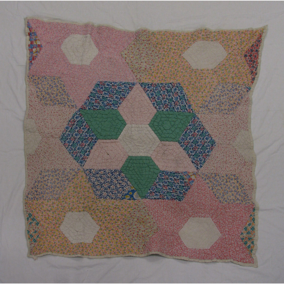 A quilt stitched of pastel pink, orange, and cream fabric with an accent portion in the middle in blues and greens.