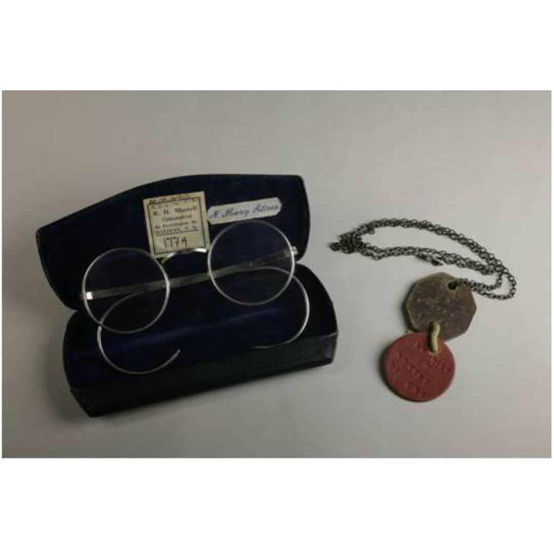 A pair of vintage glasses in a glasses case, and a set of military dog tags on a chain.