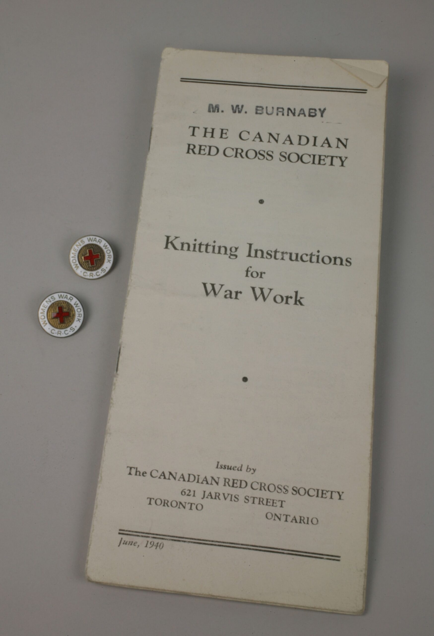 A Canadian Red Cross Knitting Instructions for War Work booklet, with two lapel pins beside it.