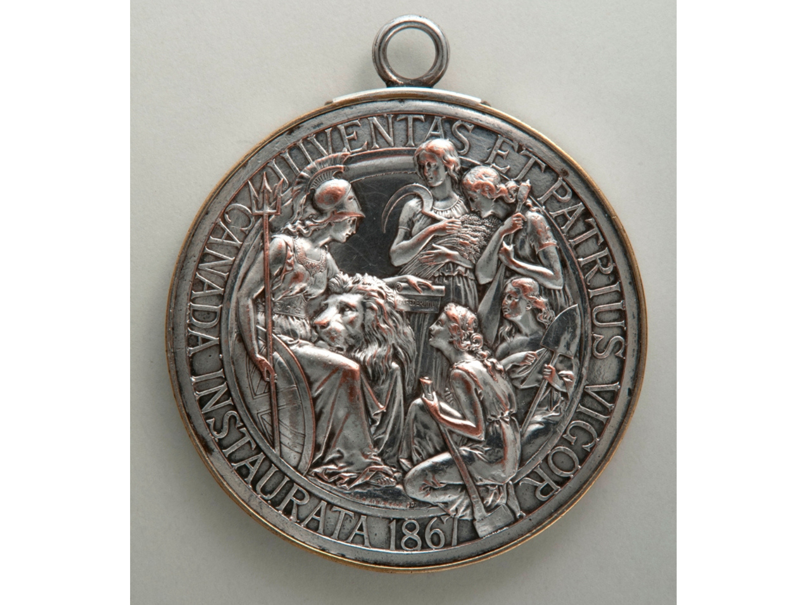 Close up of a Confederation medal showing "Britannia" wearing a helmet and with a lion at her feet resting its head on her knee, surrounded by four women.