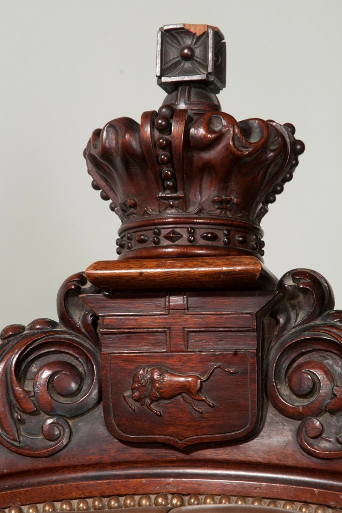 Detail f the wooden crest rail along the back of the arm chair. Displays a crest containing the cross of St George with a running bison below it, and a crown atop the crest.