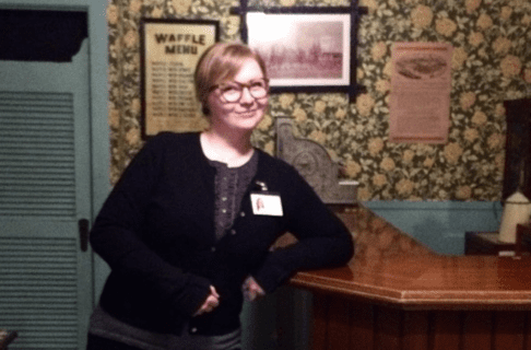 A young adult posing for a photo while leaning against the bar of the Urban Gallery cafe in the Manitoba Museum.