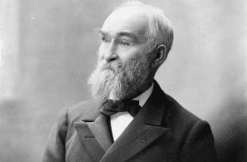 Formal black and white posed photograph of John Macoun, an older man wearing a suit and bow tie, with a full beard, bushy eyebrows, and hair thinning on top.