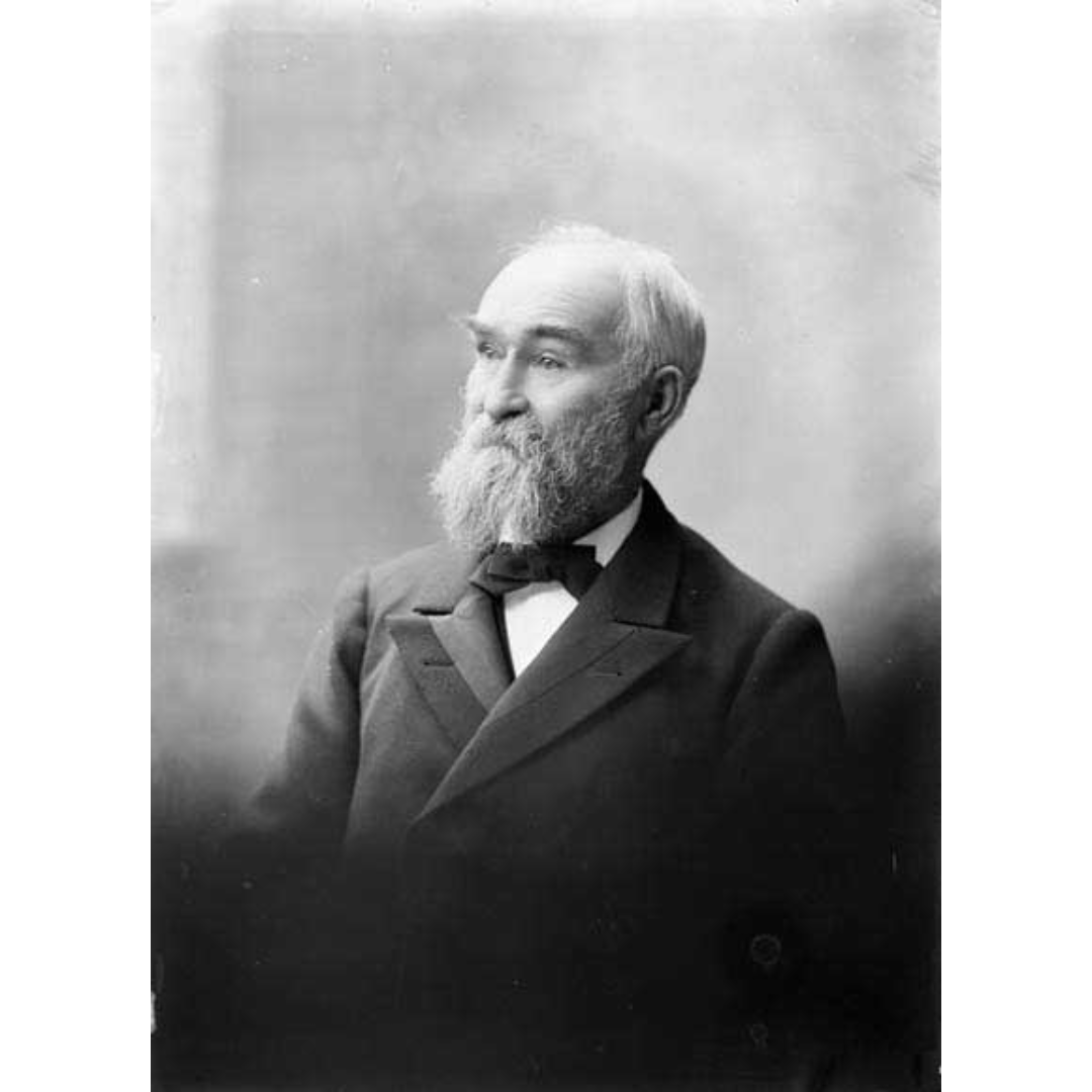 Formal black and white posed photograph of John Macoun, an older man wearing a suit and bow tie, with a full beard, bushy eyebrows, and hair thinning on top.