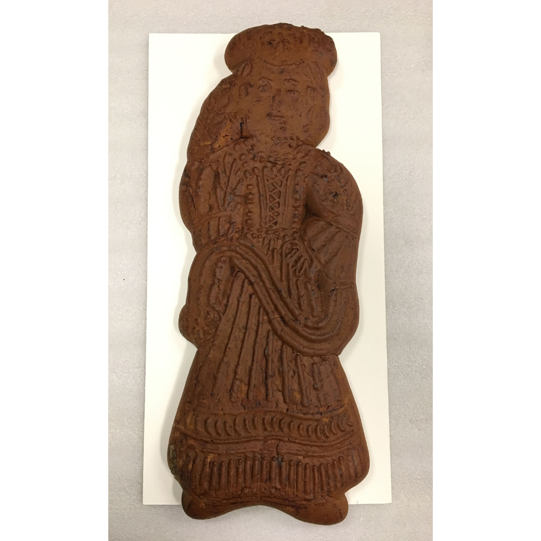 A preserved, decorative loaf of brown bread. A figure wearing a laced dress and hat.