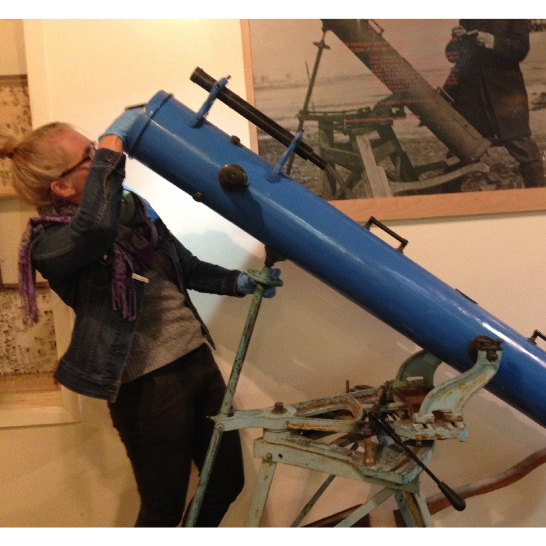 Carolyn standing at the front of a blue telescope, examining the front opening, while wearing blue gloves.