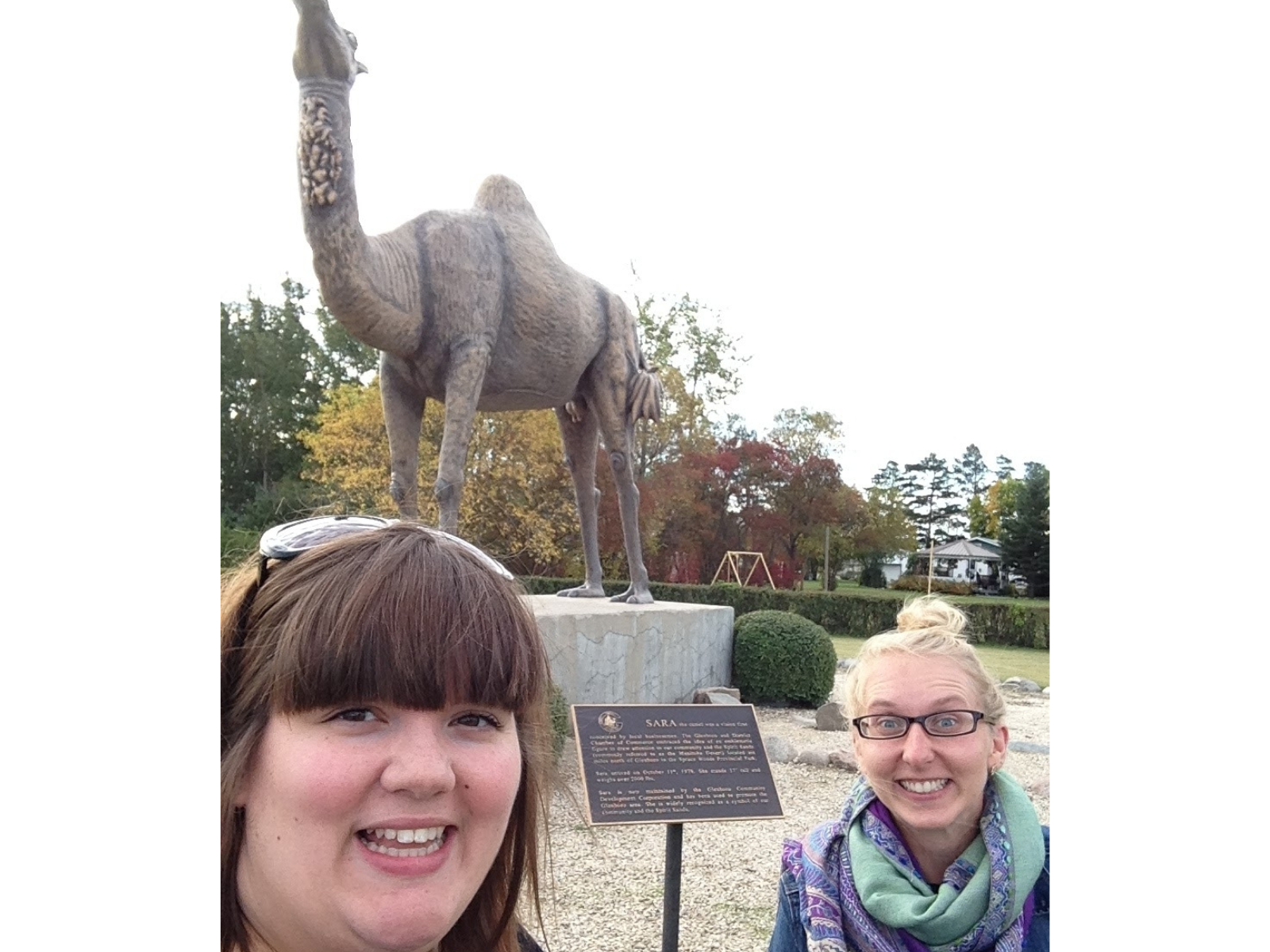 A smiling selfie taken by Cortney of herself and Carolyn in front of a statue of a giant single-humped camel.