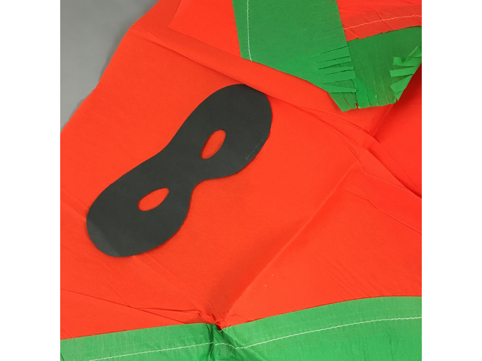 Close-up on elements of a crepe paper Halloween costume in orange and green, with a black eye mask.