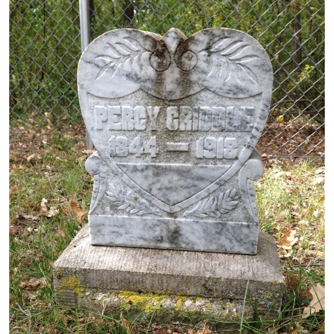 A heart-shaped gravestone with two engraved leaves on the top of the heart. the stone reads, "Percy Criddle / 1844 - 1918".