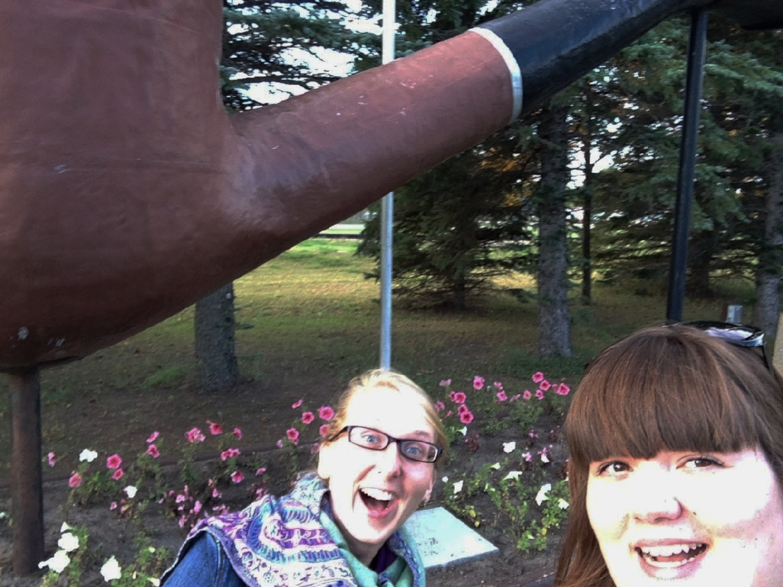 A smiling selfie taken by Cortney of herself and Carolyn in front of a giant brown and black smoking pipe statue.